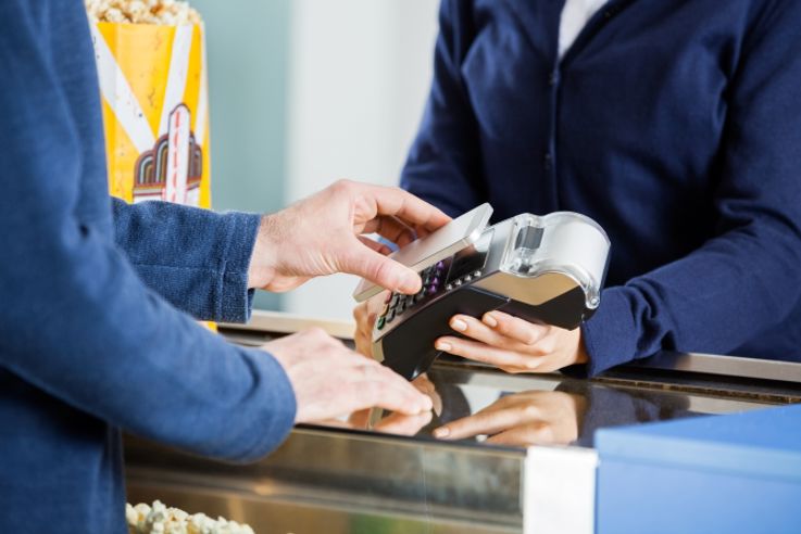 Midsection of man using NFC technology to pay bill at counter